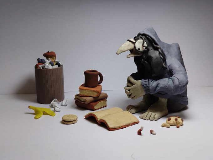 A claymation-style scene features a hooded, skeletal figure sitting next to a trash can overflowing with food scraps, with a stack of books, a mug, a banana peel, and cookies scattered on the ground.