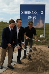 Three men in suits holding shovels at a groundbreaking ceremony in front of a blue sign reading 'STARBASE, TX 69420'.