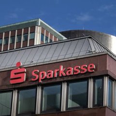 The image shows a Sparkasse bank building with the red “Sparkasse” logo and name prominently displayed. It relates to the accompanying post about Sparkasse’s banking network rolling out cryptocurrency trading through its app.