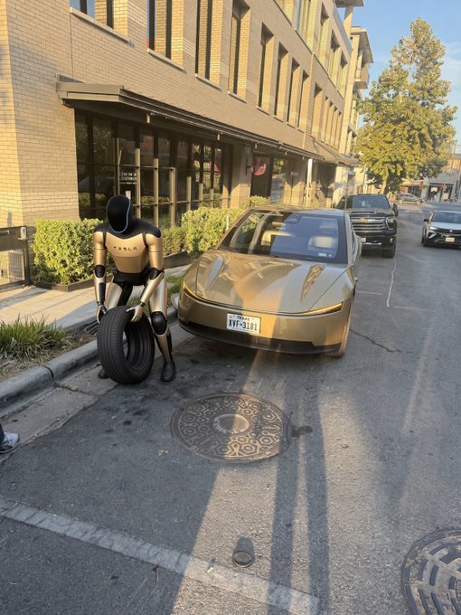 Street scene showing a Tesla (with Texas plate 'HYF-3161') parked next to a humanoid Tesla Optimus robot that is holding a tire, with other vehicles visible in the background.
