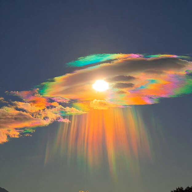 The image features a beautiful, colorful rainbow that appears to be falling from the sky. The sun is shining brightly behind the rainbow, creating an awe-inspiring sight. The vibrant colors of the rainbow are spread across the sky, making it a captivating scene for viewers.