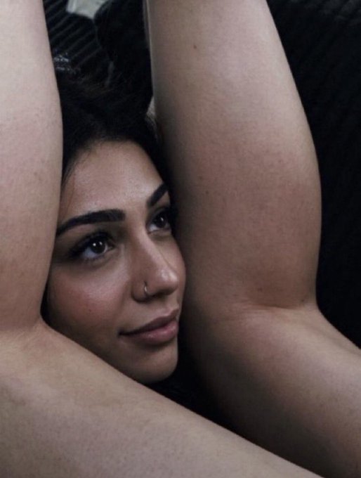 A woman with dark hair and a nose ring rests her face between her bare arms, gazing softly at the camera with a subtle smile. The playful caption about Crypto Twitter complements the cheeky, teasing mood of the suggestive photo, as if she's enjoying the wild ride of crypto drama.
