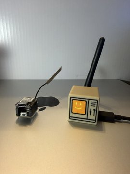 The image features two small electronic devices placed side by side on a table. One device appears to be a toy or a small robot with a smiley face design, while the other seems to be a radio control unit (RCU) connected to a power cord. The RCU has an antenna attached to it, which is likely used for communication purposes. The image also includes text that reads "silly @bankrbot, what are you doing as a @ratspeakorg node?". This suggests that the RCU might be part of a toy or a small robot designed with an RCU functionality and possibly connected to a power source through a cord.