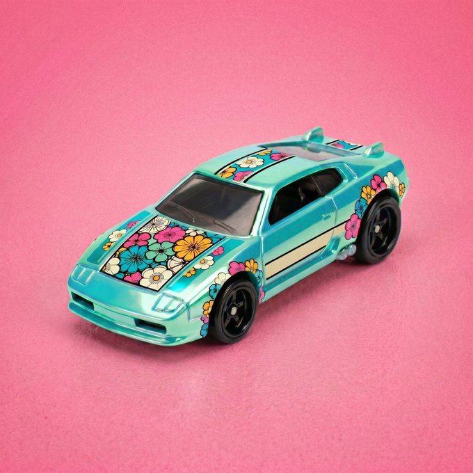 A teal toy car adorned with colorful floral decals sits against a bright pink background, showcasing the customizable "skins" design feature enabled by the ERC-7160 multi-media contract from @TransientLabs. The vibrant flower patterns on the vehicle demonstrate the platform's flexibility for minting additional aesthetic variations onto existing Racers.