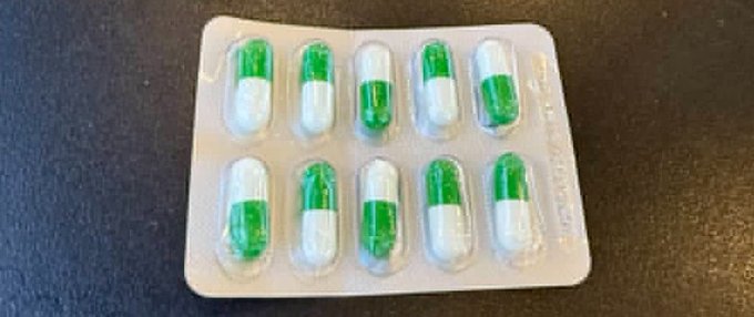 A blister pack containing ten green and white pharmaceutical capsules arranged on a dark surface.