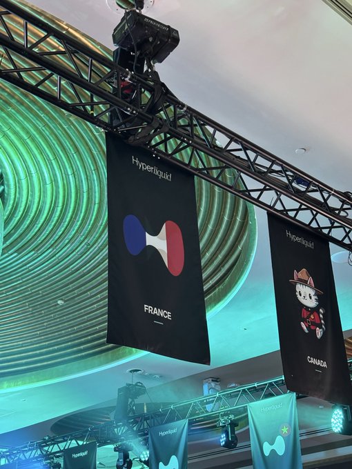 Banners hanging from the ceiling at a conference display "Hyperliquid" country branding for France and Canada, marking the crypto platform's growing international presence as celebrated in the caption "Mom we made it to Hyperliquid's hall of fame."