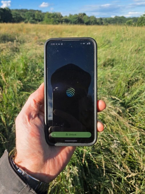 The image shows a person holding up their phone, which has an app icon displayed that reads "Jupiter". This suggests that the user might be trying out or testing the app's functionality related to Jupiter. The phrase "proof of touching grass" could possibly be a metaphor for the user experiencing the app in real-life situations, such as using it outdoors while holding their phone and interacting with the app icon on the screen.