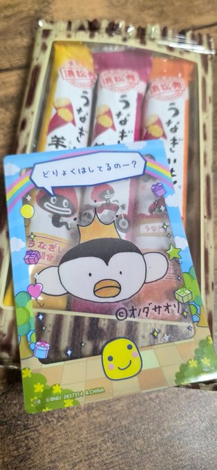 The image features a cute cartoon penguin face card, which has been cut out from an envelope or package with Japanese writing on it. The card is placed next to another envelope that also contains a picture of a cartoon penguin. The background appears to be a wooden surface, and there are some stars visible in the scene as well.