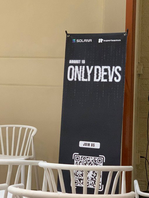 A black banner at the OnlyDevs Vietnam event displays "AUGUST 15," "ONLYDEVS," and "JOIN US" alongside logos for Solana and SuperteamVN, with a QR code below. White chairs are arranged in front of the banner, which promotes the Solana-backed developer gathering.