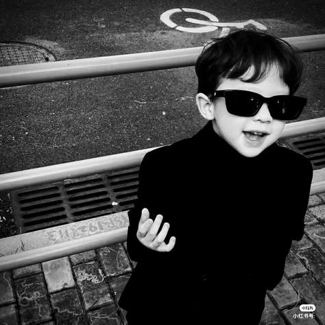 A black and white photo of a young boy wearing sunglasses and a black outfit, with a small '小红书号' (Xiaohongshu ID) watermark in the corner.