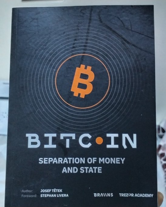 The image features a book titled "BITCOIN - Separation of Money and State" by José Tezk, published by Trezor Academy. The book cover displays an orange Bitcoin symbol, indicating that the content inside might be related to Bitcoin or cryptocurrency. The book is being promoted at a Bitcoin conference in Nairobi, Kenya, as seen from the image.