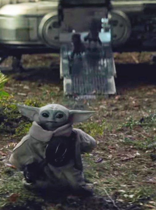 A scene featuring Grogu (Baby Yoda) sitting on the ground in front of a spaceship ramp in a forest setting.
