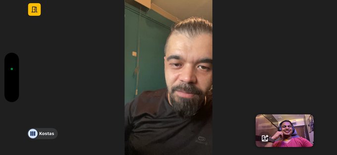 A video call interface showing a bearded man in a black shirt labeled 'Kostas' in the main view, with a smaller picture-in-picture window showing a smiling woman in a pink shirt.