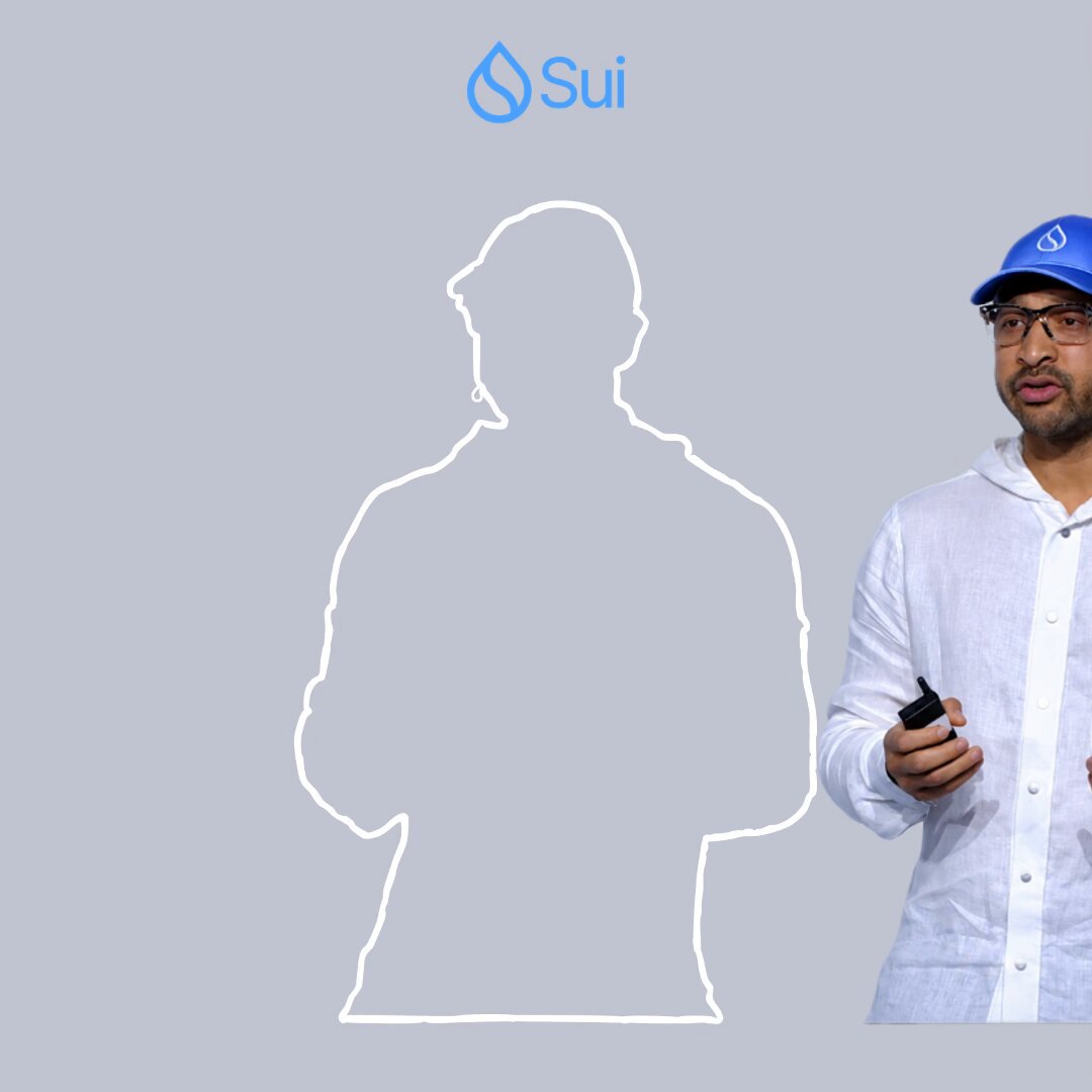 The image features a man wearing glasses standing next to a gray wall with a white background. The man has his arms crossed over his chest as he poses for the photo. There are no other people or objects visible in the image, making him the sole focus of the picture.