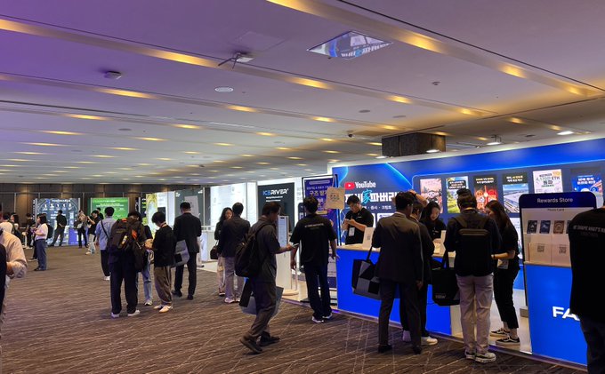 A crowded tech conference or expo floor with attendees gathered around booths including YouTube and a 'Rewards Store', suggesting a gaming or streaming event.