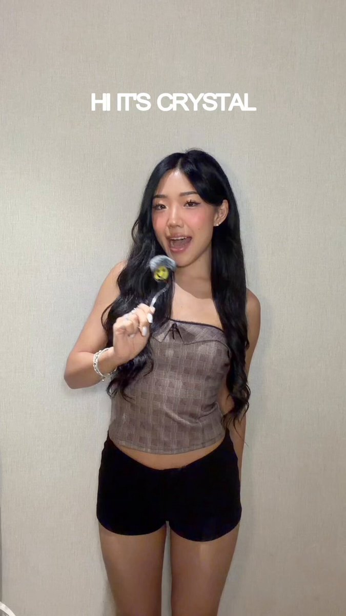 The image features a woman standing against a white wall, holding a lollipop up to her mouth with both hands. The background of the photo is blurred, drawing attention to the woman and her action. The caption for this image reads "WEEKLY RAPID CRYPTICO NEWS DROP @solana EDITION: Ep. 26".