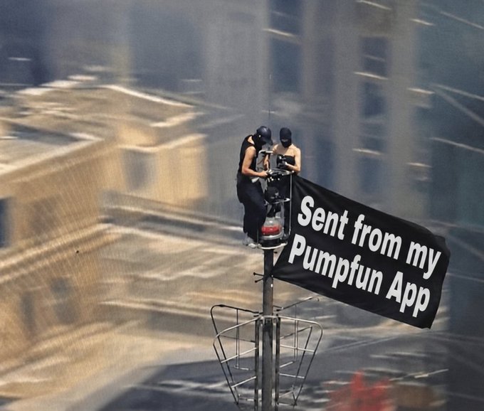 Two masked individuals perched precariously atop a broadcast tower unfurl a black banner reading "Sent from my Pumpfun App," humorously staged as if checking crypto charts required scaling dangerous heights—just like the bold tagline promised in the caption.