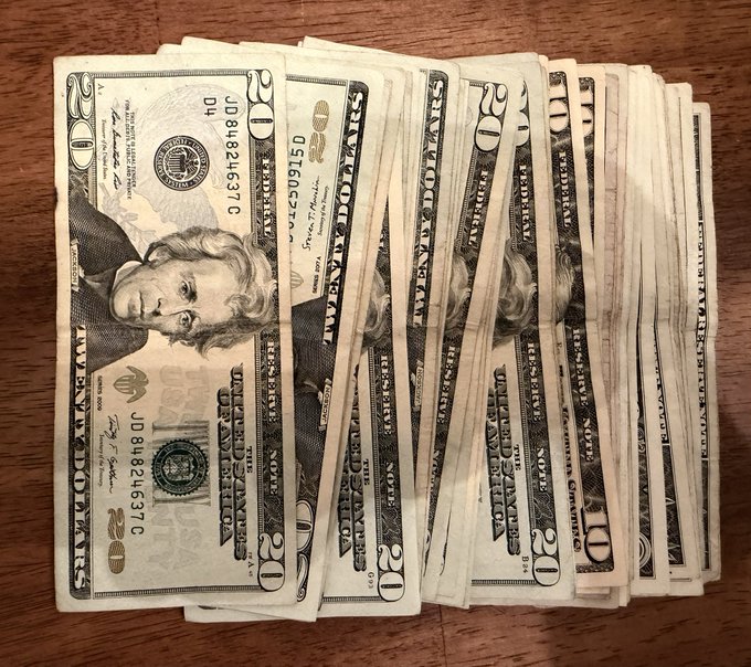 A fanned-out stack of US $20 bills on a wooden surface, showing Andrew Jackson's portrait.