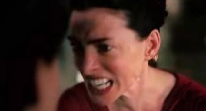 A close-up of a woman with short dark hair, her face contorted in an intense, frustrated expression as she bares her teeth, seemingly in mid-yell or grimace. The image humorously captures the exasperated reaction of someone struggling to solve a CAPTCHA test featuring buses and traffic lights.