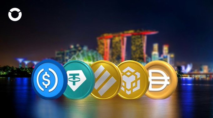 Five cryptocurrency coins displayed in front of the Singapore Marina Bay Sands skyline at night, featuring USDC, Tether, Solana, BNB, and Dai logos.