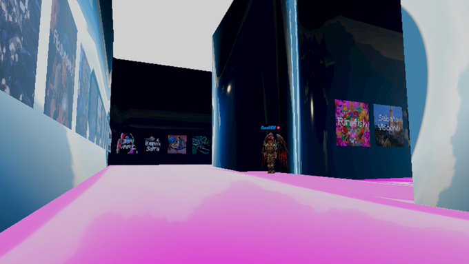 A screenshot from a 3D virtual world or game showing a character with angel wings standing in a corridor with framed artwork on the walls and a pink carpeted walkway.