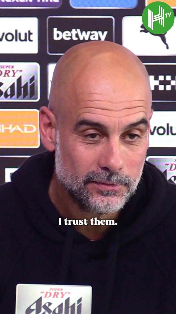 Pep Guardiola, bald with a gray beard and wearing a black hoodie, is captured in a close-up shot during what appears to be a press conference, with sponsor logos including "betway," "Etihad," "Asahi," and "Evolut" visible in the background. The caption "I trust them" is displayed on screen, aligning with his reported comments expressing trust regarding Manchester City's charges as he prepares to leave the club.