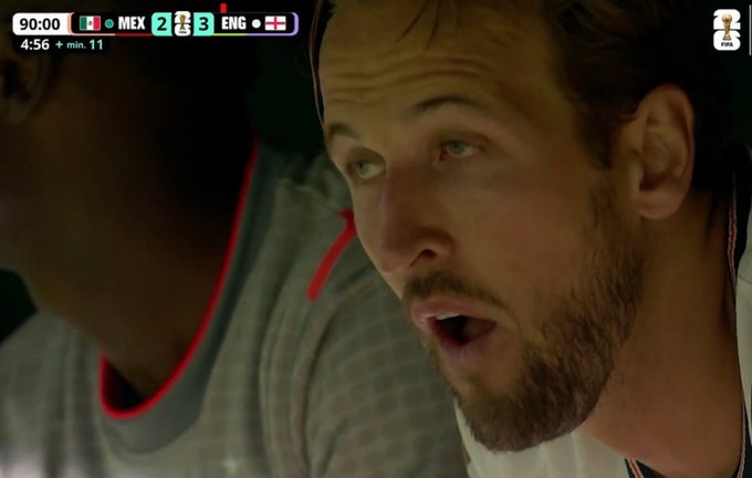 A close-up shot of a bearded man with his mouth open in shock, overlaid with a World Cup soccer scoreboard showing MEX 2 - 3 ENG at 90:00 with 6 minutes of stoppage time—suggesting a last-minute goal that would leave Mexico fans stunned, mirroring the post's theme of crypto enthusiasts reacting to bad news about Michael Saylor selling Bitcoin.