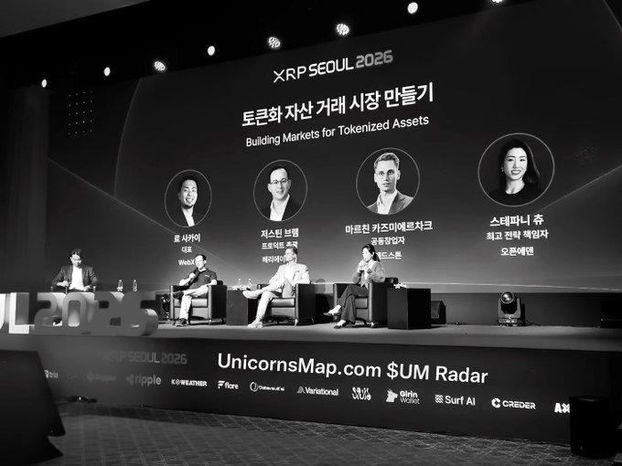 A black and white photo captures a panel discussion at the 'XRP SEOUL 2025' event titled 'Building Markets for Tokenized Assets,' featuring four speakers on stage.