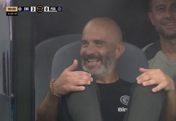 A man sporting a Chelsea t-shirt and beaded bracelet smiles broadly and gives a thumbs up while seated next to another person. The scoreboard reads "CHE 3 PSG 0" at the 90:00 mark with 5 added minutes, suggesting Chelsea's decisive lead mirrors the poster's excitement about a profitable trading win.