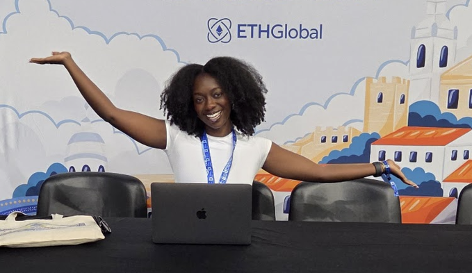 A smiling woman with curly hair stands behind a table with an open MacBook, arms outstretched, against a backdrop featuring the 'ETHGlobal' logo and illustrations of buildings.