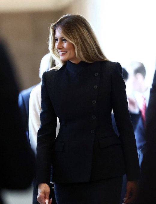 Photo of a blonde woman wearing a black buttoned blazer and turtleneck, smiling in what appears to be a formal setting.