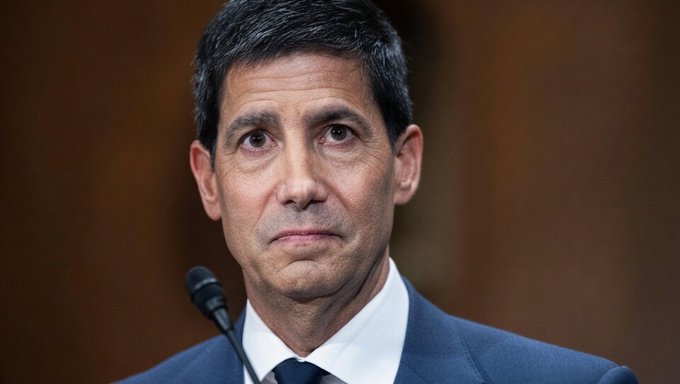 A man in a dark blue suit and tie speaks at a microphone during what appears to be a formal hearing or press conference. The image is used to illustrate the post announcing the Federal Reserve's decision to leave interest rates unchanged at 3.50%–3.75%.