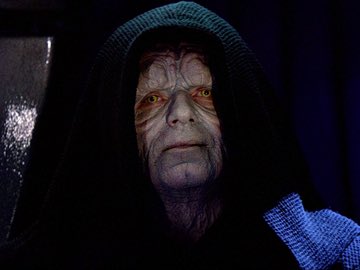 A close-up of Emperor Palpatine from Star Wars wearing a dark hooded robe, with his distinctive scarred face and yellow eyes visible.