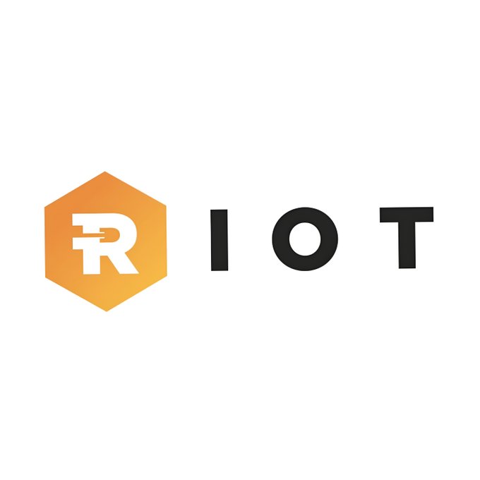 The image displays the Riot Platforms logo, featuring an orange hexagon with a stylized white "R" alongside the bold black text "RIOT," representing the Bitcoin mining company ($RIOT) mentioned in the post about its recent sale of 4,300 BTC to fund operations and data center expansion.