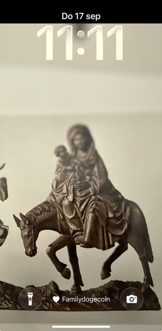 An iPhone lockscreen dated 'Do 17 sep' at 11:11, displaying a sepia-toned statuette of Mary holding baby Jesus while riding a donkey, with the handle '@Familydogecoin'.