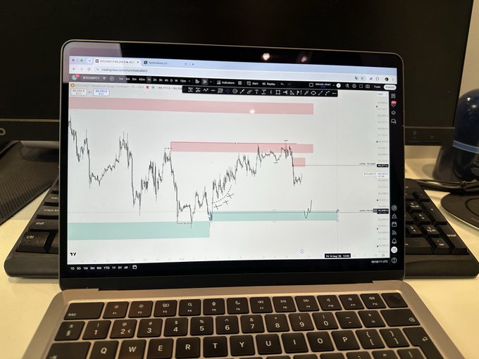 A laptop screen displays a financial trading chart with red and green zones, showing BTCUSDT.P price action on the Bybit platform.