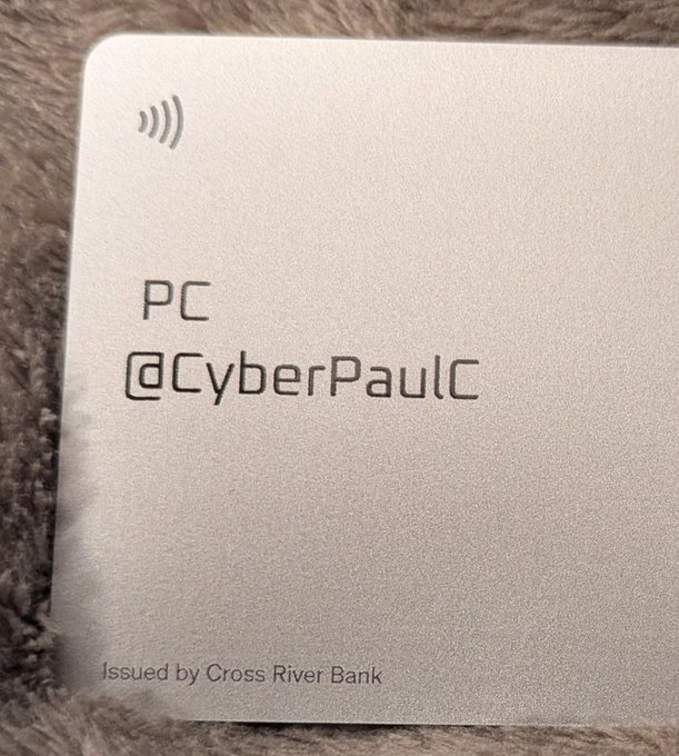A close-up of a silver metal card displaying 'PC @CyberPaulC' and 'Issued by Cross River Bank' with a contactless payment symbol.
