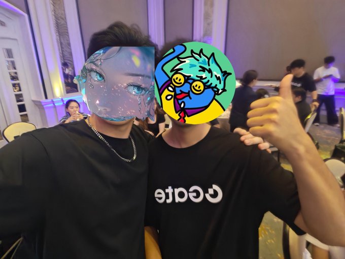 Two people pose together at an indoor event, one wearing a black Coinbase t-shirt, with their faces covered by digital stickers of anime-style and cartoon characters.