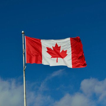 The Canadian flag waves against a blue sky, symbolizing the nation at the center of a major banking initiative as its six largest banks—BMO, CIBC, National Bank, RBC, Scotiabank, and TD—collaborate on tokenized Canadian-dollar deposits to modernize cross-bank transactions.