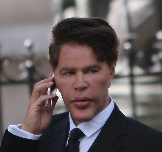 A sharply dressed man in a black suit, white shirt, and dark tie holds a smartphone to his ear with a serious, focused expression, seemingly monitoring a developing situation. His attentive demeanor and professional attire align with the post's ominous "new swarm detected?" caption, suggesting he is being briefed on an urgent threat.