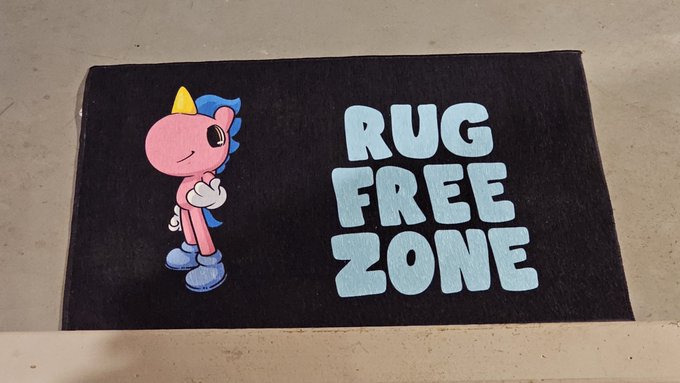 A black rug or mat featuring a cartoon unicorn character alongside the text 'RUG FREE ZONE' in light blue lettering.