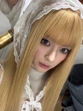 A close-up photo of a woman with blonde hair wearing a white lace headpiece and a white turtleneck top.