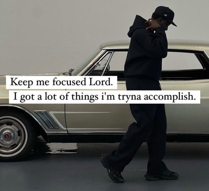 A person in a black hoodie and cap walks past a classic car, with text overlay reading: 'Keep me focused Lord. I got a lot of things i'm tryna accomplish.'