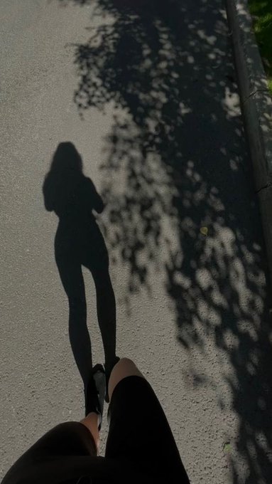 The shadow of a person taking a photo is cast on the pavement, alongside their feet in black sneakers and leggings.