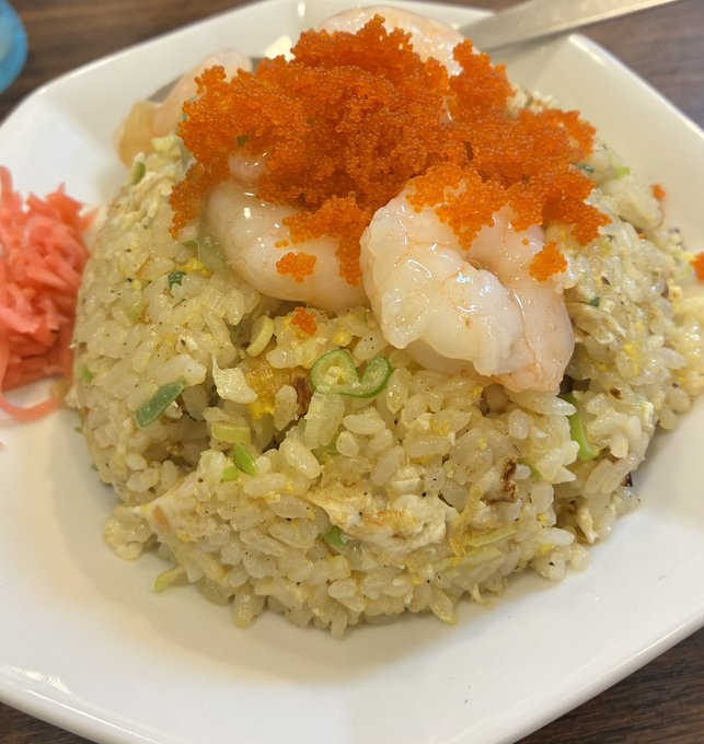 The image shows a white plate filled with rice, shrimp, and orange slices. There are also some green vegetables mixed into the dish. The plate appears to be placed on top of a dining table. The photo has been captioned "海老チャー #STEPN".