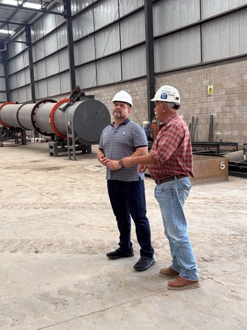 Two men in hard hats (one wearing a "COPA" branded cap) stand inside an industrial facility beside large cylindrical equipment, with the number "5" visible on a beam behind them, reflecting the $AABB post's enthusiasm about checking in on the company's operations.