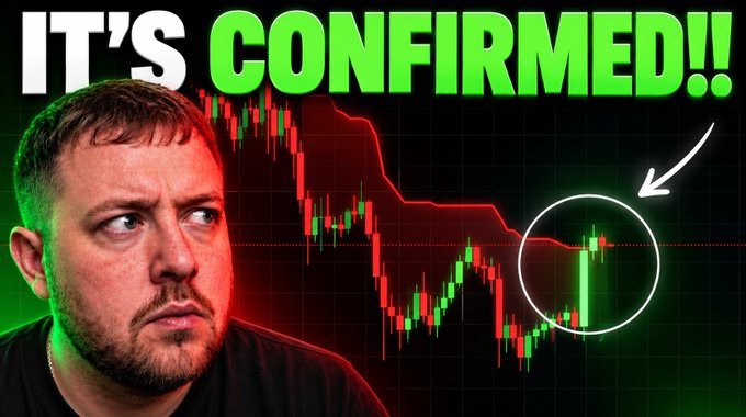 The image is a YouTube thumbnail featuring a man with a serious expression alongside a Bitcoin price chart showing red and green candlesticks in a downward trend, highlighted with a white circle and arrow. The bold green and white text "IT'S CONFIRMED!!" dominates the top, promoting the video's claim about Bitcoin. The thumbnail aligns with the post's announcement of confirmed Bitcoin news and a $100 giveaway comment contest.