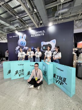 A person crouches in front of a Bitget promotional booth at Taipei Week, displaying signage that reads "ONE WORLD, ALL ASSETS" and "Bitget #来了就是VIP" alongside Bitget branding and a mascot. The post references encountering @phyrexni filming with Ray-Ban glasses at the event, tying into the crypto exchange's promotional presence.