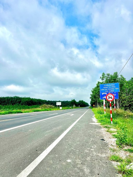 The image shows an empty street with a blue sky above and trees lining both sides of the road. There are no cars or people visible, giving off a sense of tranquility and peace. The caption reads "New week, full of energy, everyone! Waking up each day is a chance for us to conquer new heights The grind to make a living keeps going, the road' blocked for the new car". This message seems to be related to the post about the car being stuck in traffic on the highway.