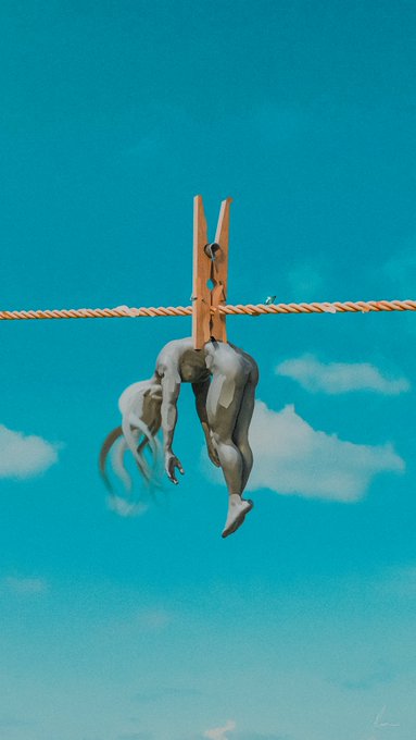 The image features an orange clothespin with a white figure hanging from it, suspended by a rope against a blue sky background. The figure appears to be a person or a sculpture of a person, possibly made of metal or stone. The text "Hanging in there Pulling through in a big world." is present in the image as well.